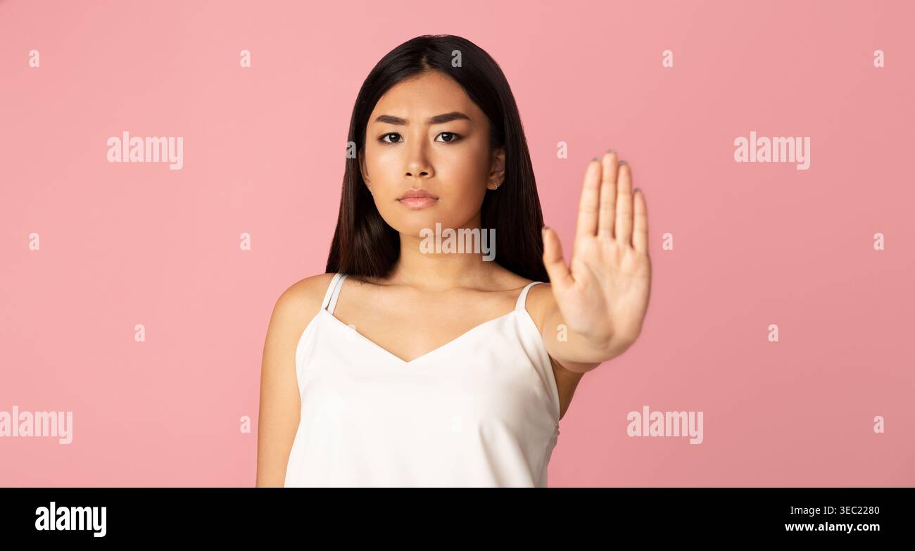 Jeune femme exprimant un Stop Gesture sur un fond rose pendant un moment de calme Banque D'Images