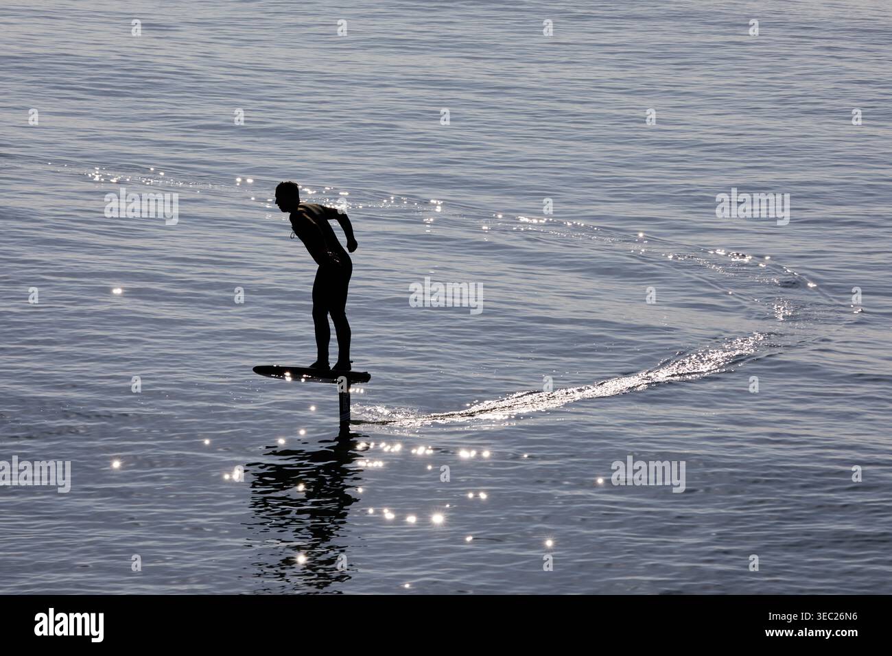 Un surfeur se déplace à travers la mer du matin, en équilibre sur une planche de surf en hydrofoil. Les planches d'hydroptère utilisent une aile pour le levage, permettant de glisser au-dessus de l'eau. Banque D'Images