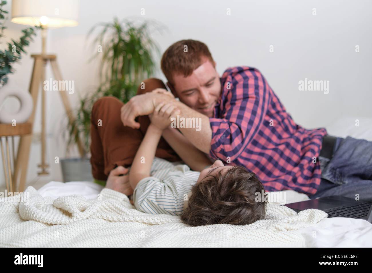 Parent et enfant joyeux appréciant le temps chatouillant dans la chambre, rayonnant de joie et un lien familial fort. Père chatouillant son fils sur le lit, partageant Banque D'Images