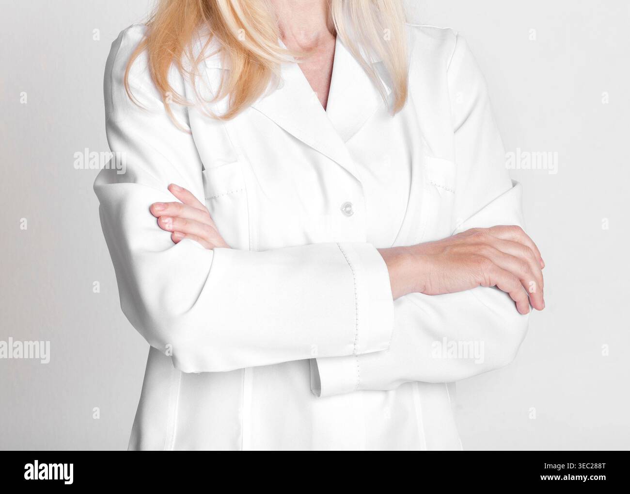 Travailleur de la santé professionnel portant un manteau blanc avec les bras croisés sur un fond Uni Banque D'Images