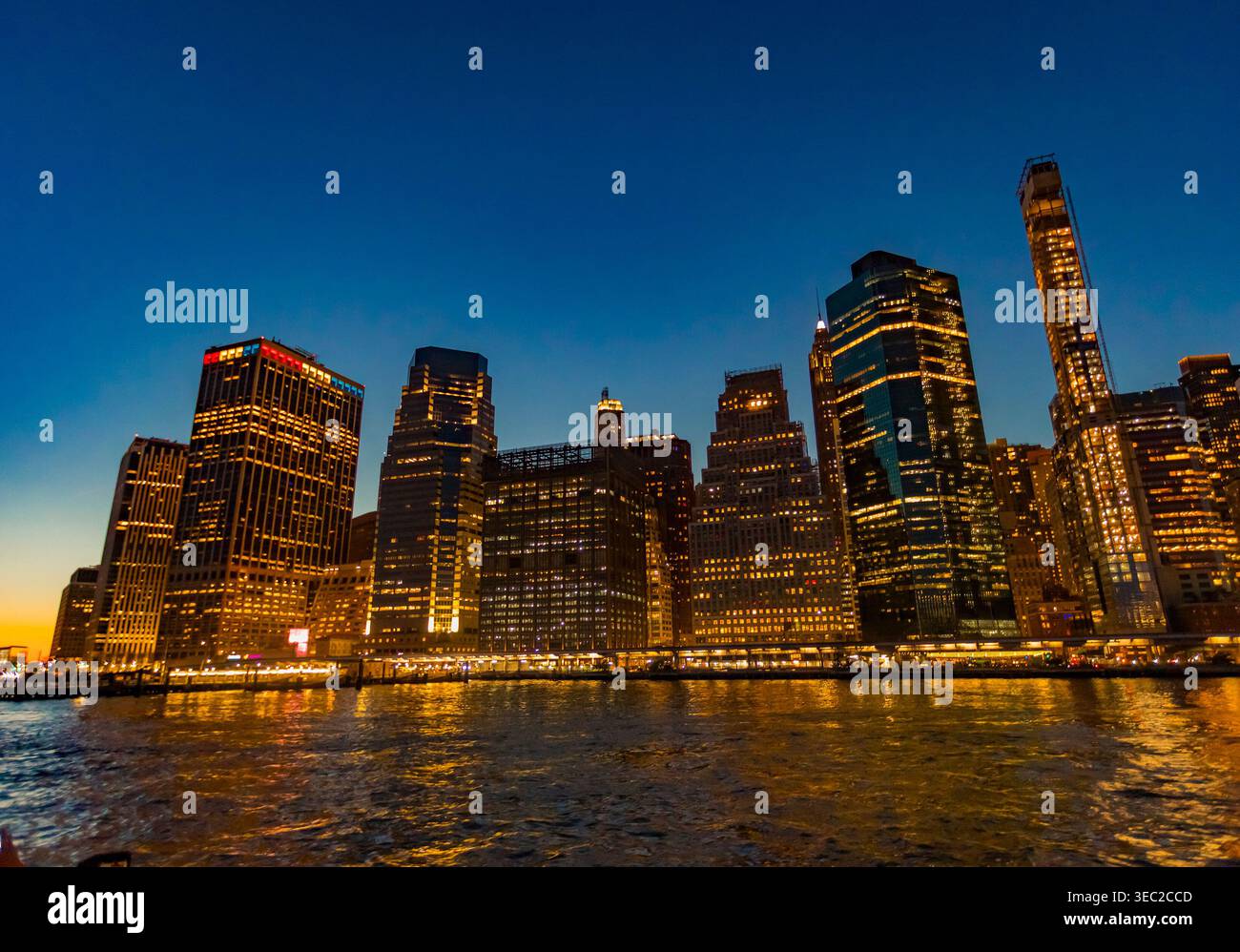 Lower Manhattan scintille de lumières vibrantes au crépuscule. Les gratte-ciels se dressent contre un ciel bleu profond, reflétant l'énergie de la ville. Banque D'Images