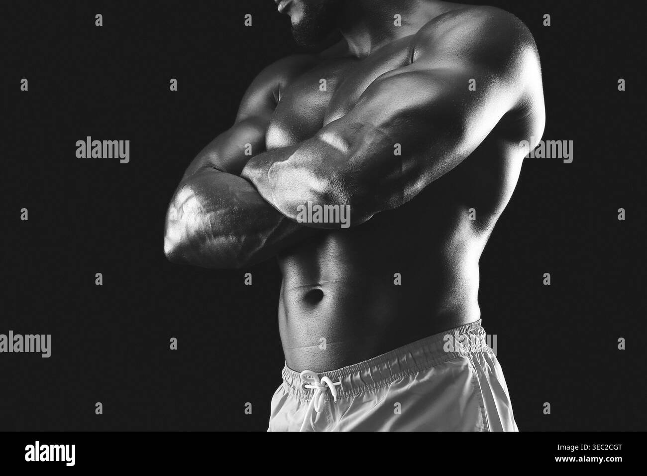 Musclé homme pose avec confiance, les bras croisés dans un décor noir et blanc dramatique Banque D'Images