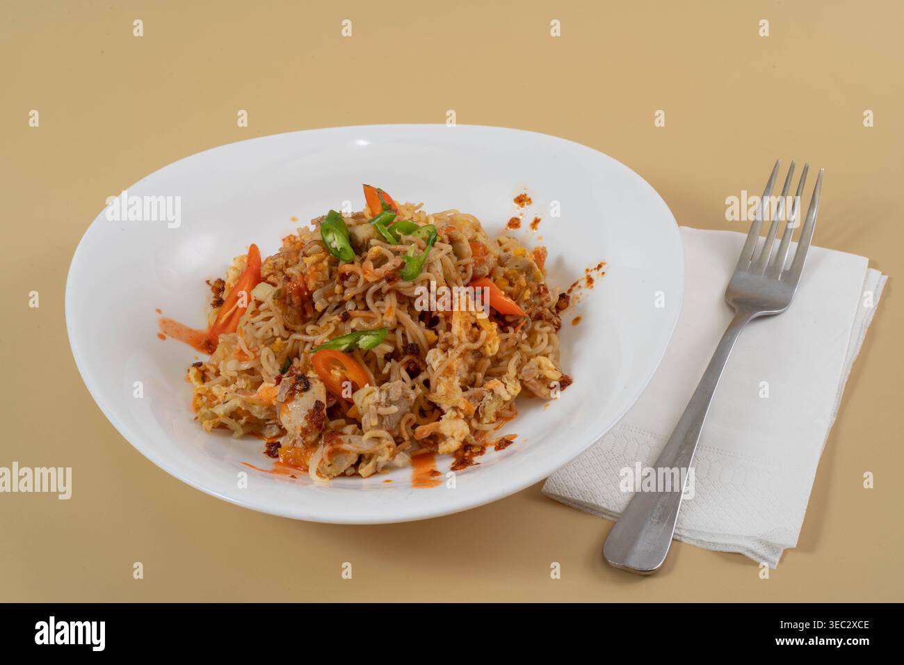 Nouilles asiatiques sautées épicées servies dans un bol blanc avec une fourchette en métal et une serviette sur le côté. Délicieux plat de nouilles au poulet, shot studio. Banque D'Images