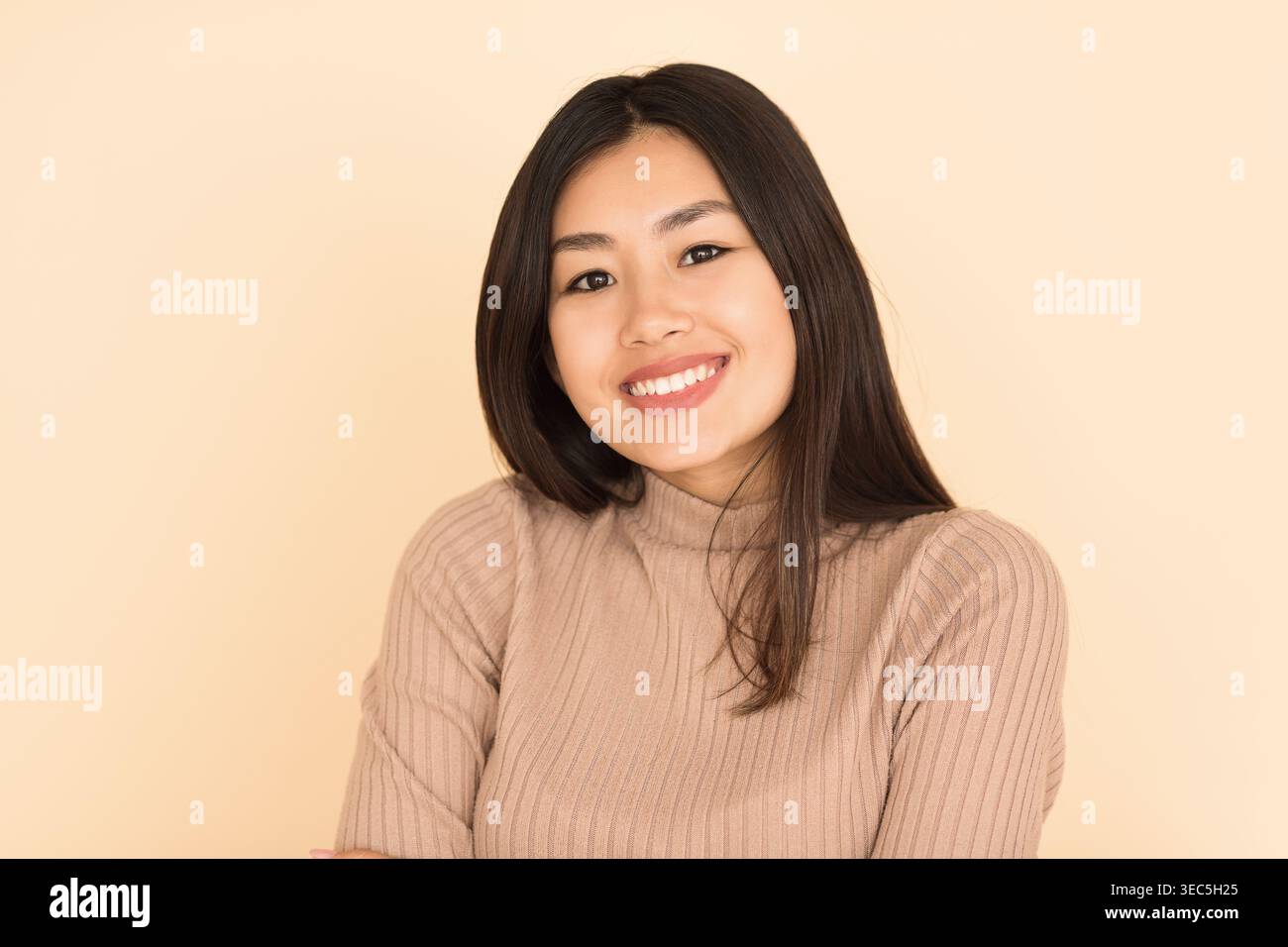 Sourire jeune femme avec de longs cheveux noirs portant un pull beige sur un fond clair Banque D'Images