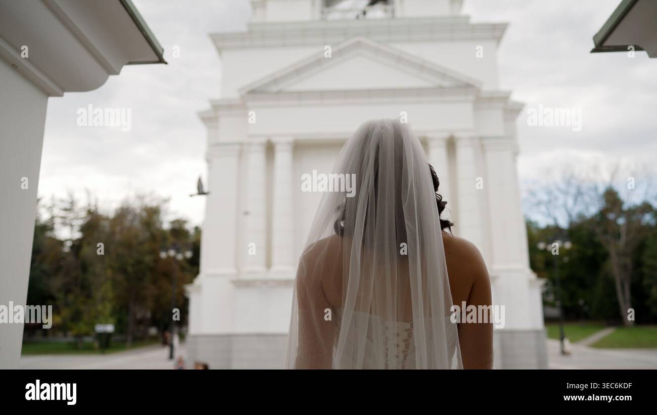 Mariée en robe de mariée et voile de derrière, debout devant un grand bâtiment classique blanc, symbolisant de nouveaux débuts Banque D'Images