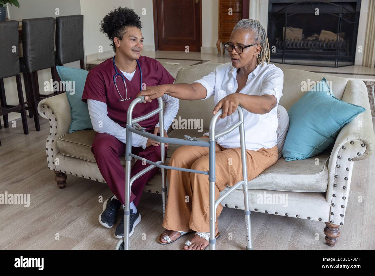 Femme afro-américaine senior assise sur le canapé à la maison à l'aide d'un marcheur, soignant dans l'observation des gommages Banque D'Images