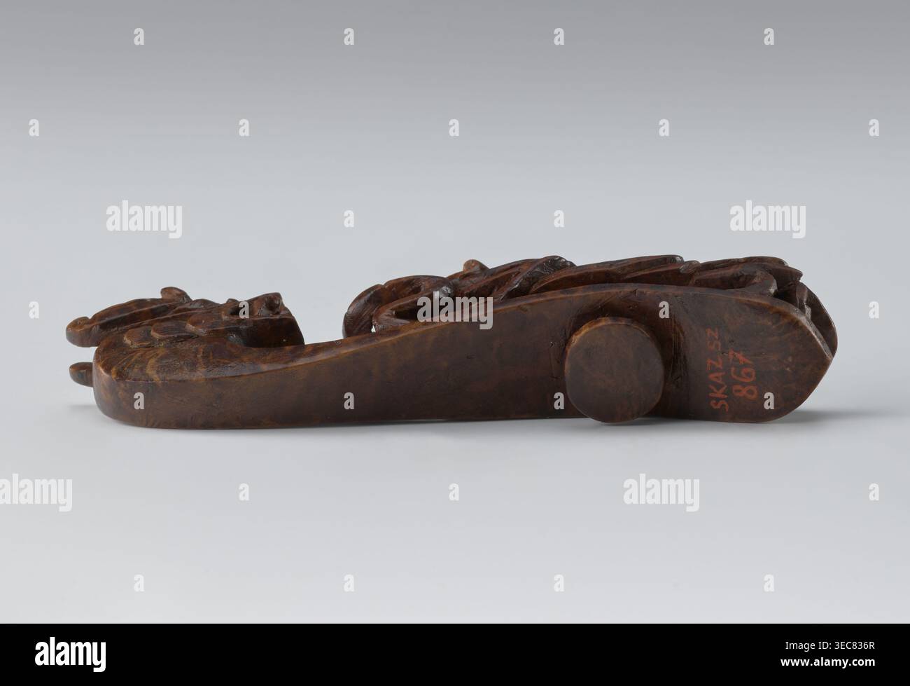 Fermoir de ceinture, chinois ; Qing 1644–1911, 19e siècle ; tige : deux dragons-lézards de combat ; tête sculptée entièrement ; tige ajourée ; matériaux : sculpté non spécifié ; fonction : ornement de vêtements/ceinture pour costume d'homme ; hauteur 3,0 cm, largeur 12,8 cm, profondeur 2,8 cm ; iconographie des dragons., un objet en bois sculpté repose horizontalement sur une surface gris pâle sur un fond dégradé gris clair ; l'objet est brun foncé avec un grain de bois varié et des détails sculptés, y compris des formes arrondies et surélevées, des côtés plats lisses et des sections sculptées texturées, et il y a une petite cheville en bois circulaire sur un côté, avec Banque D'Images