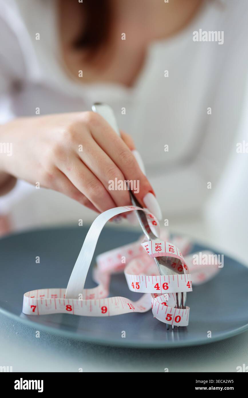 Femelle avec fourchette et ruban à mesurer au lieu de nourriture, régime toxique et concept visuel de stress nutritionnel. Banque D'Images