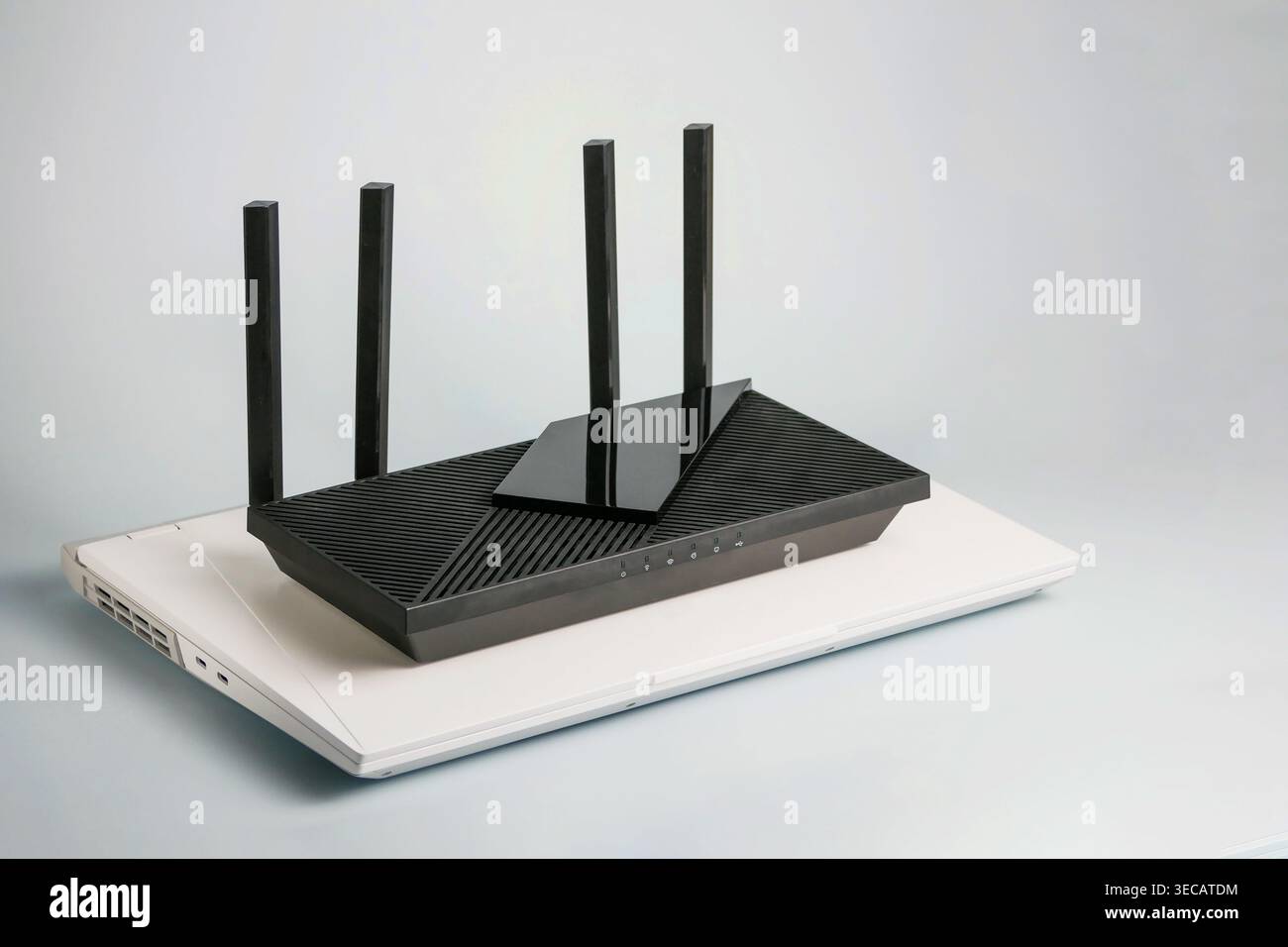 Routeur Wi-Fi noir avec quatre antennes placées sur un ordinateur portable blanc. Réseau domestique moderne, connectivité Internet et concept de configuration technologique sur BA blanc Banque D'Images