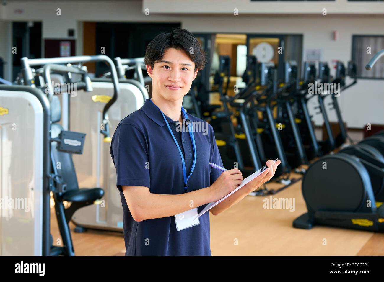 Souriant jeune instructeur japonais de gymnastique prenant des notes avec un presse-papiers Banque D'Images