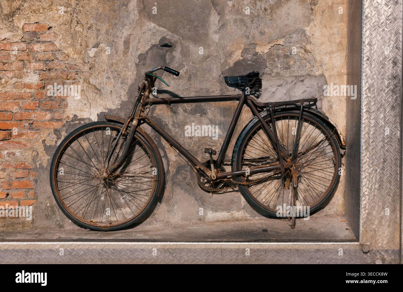 Vieux vélo rouillé appuyé contre un mur texturé de briques et de béton, mettant en valeur son charme et son usure vintage Banque D'Images