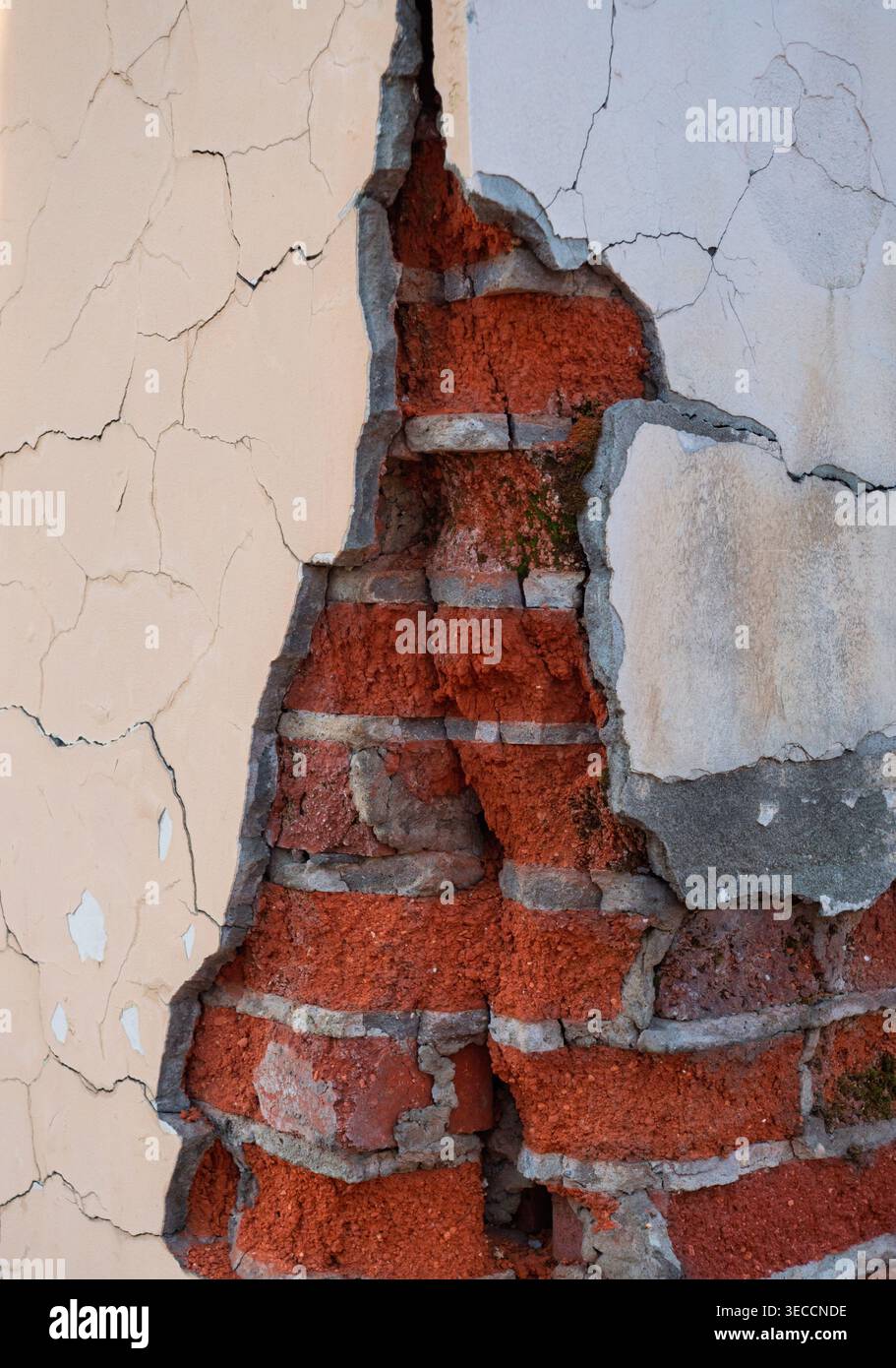 Le mur du bâtiment endommagé révèle une structure de briques rouges sous le plâtre extérieur pelé et fissuré Banque D'Images