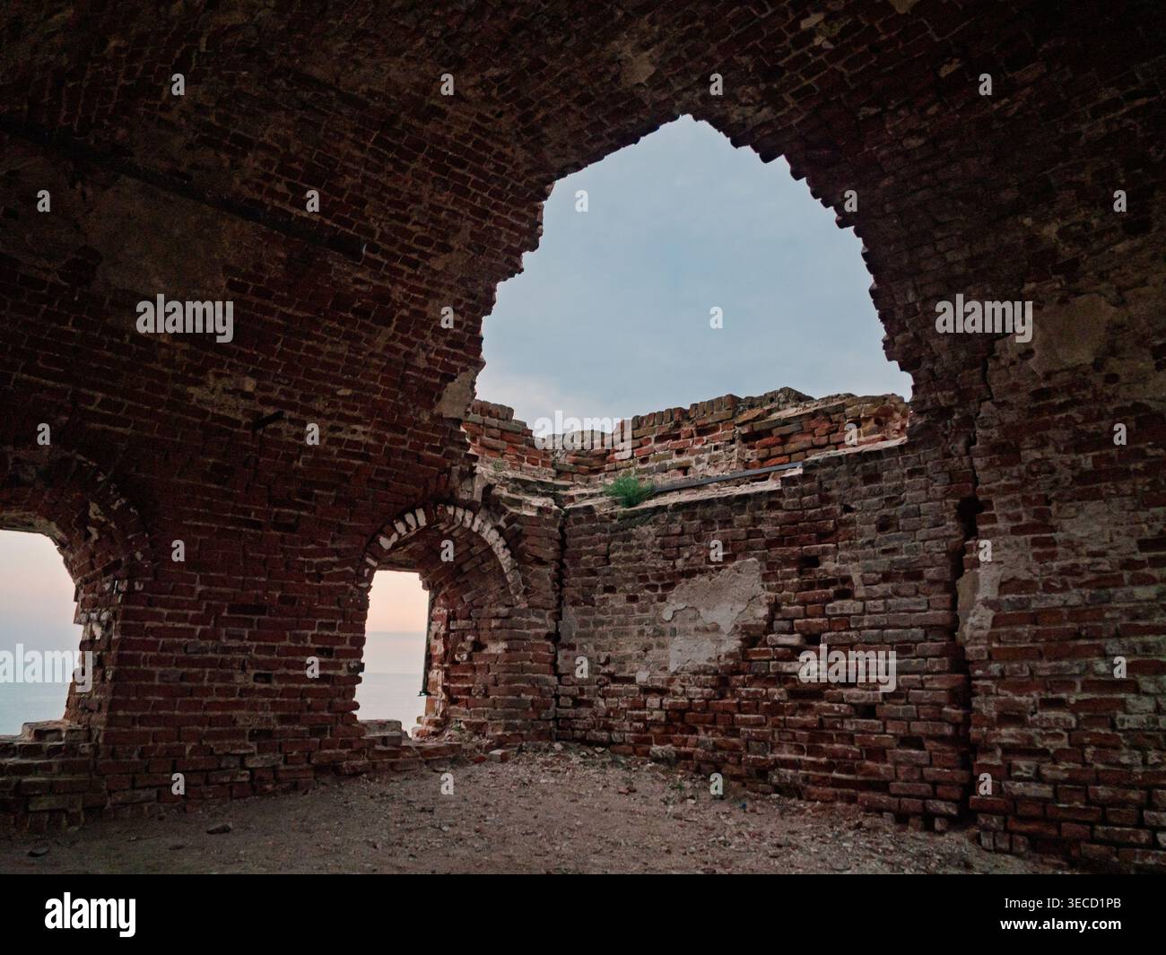 Ancien intérieur en ruine de briques avec des ouvertures voûtées encadrant l'océan et le ciel du soir Banque D'Images