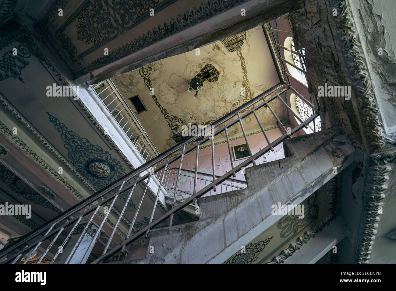 Escalier abandonné délabré vu vers le haut, balustrades ornées, plâtre écaillé, intérieur du bâtiment historique, urbex, géométrie architecturale étrange. Banque D'Images