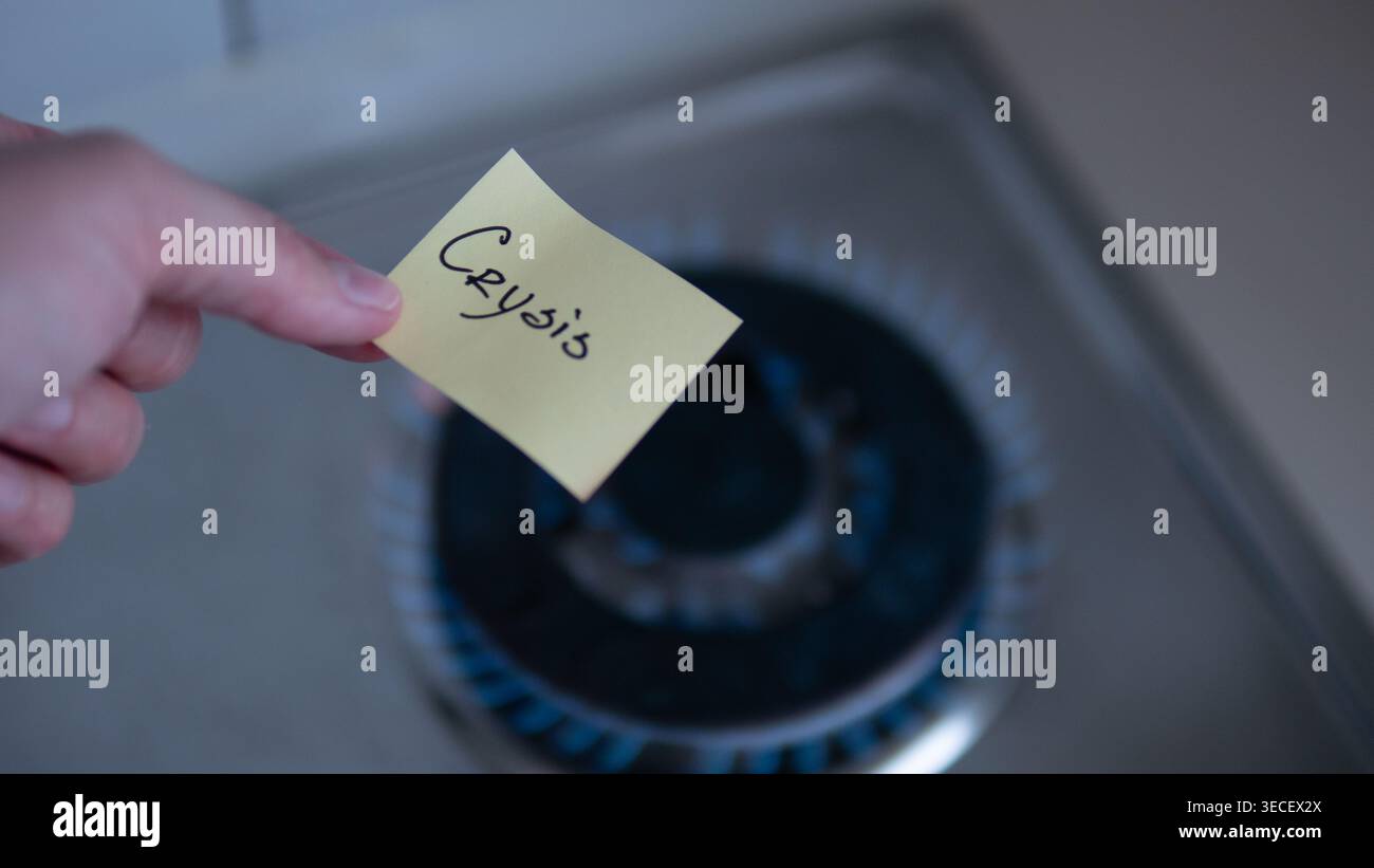 Main tenant une note collante avec le mot Crisis près de la flamme brûlante de la cuisinière à gaz. Image conceptuelle symbolisant l'inflation, la hausse des prix de l'énergie, les pénuries de gaz Banque D'Images