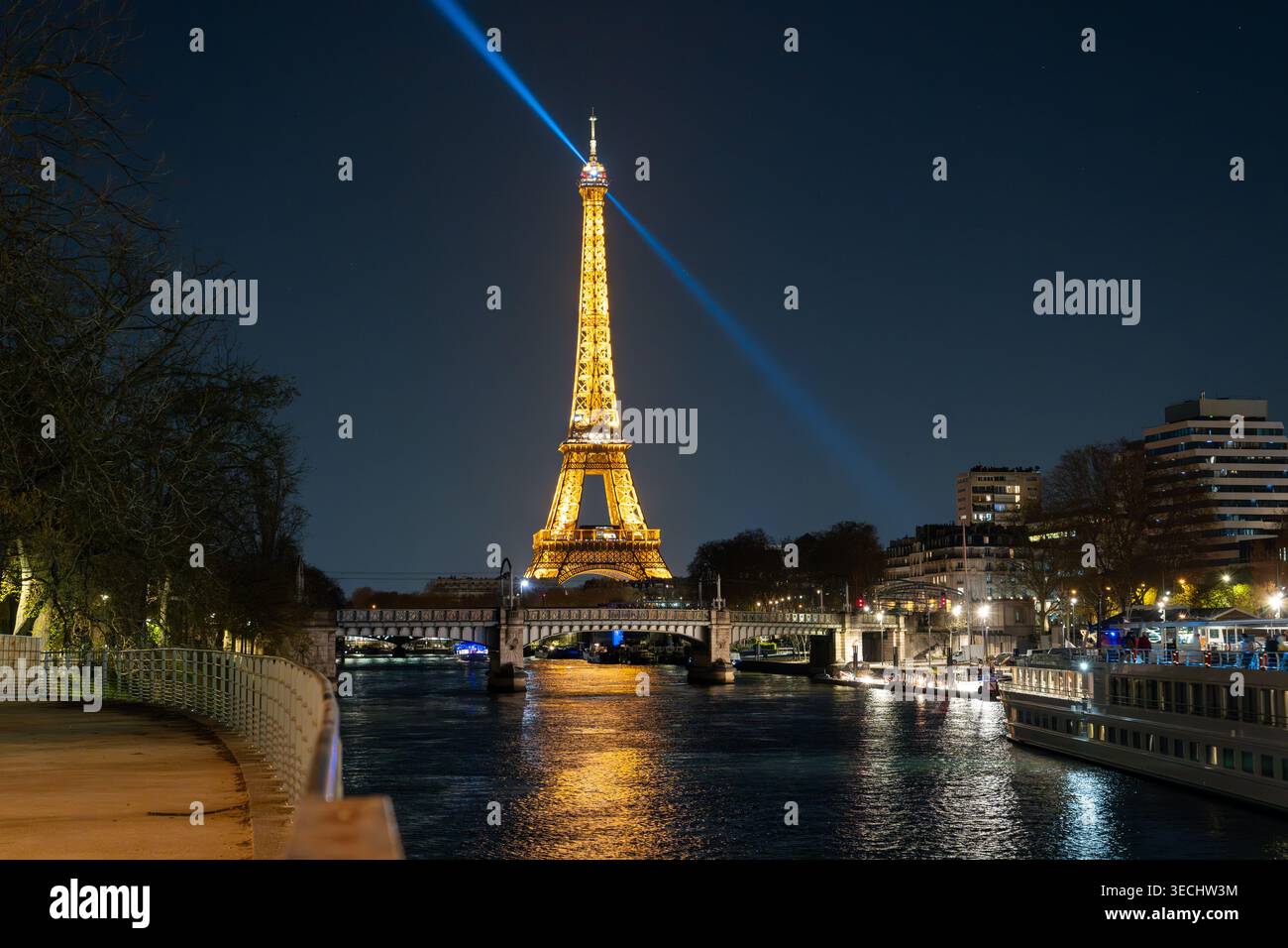 Tour Eiffel la nuit au-dessus de la Seine, vue de l'Ile aux Cygnes à Paris. La lumière de la tour s'étend à travers le ciel. Banque D'Images
