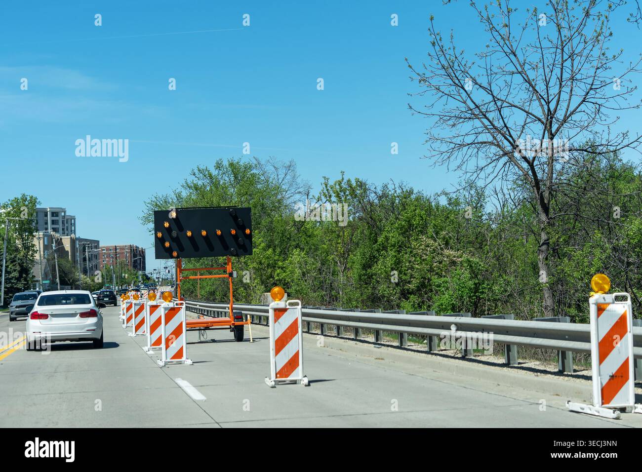 Contrôle de la circulation avec cônes et flèche électronique sur route urbaine, fermeture de voie et entretien de route en cours. Banque D'Images