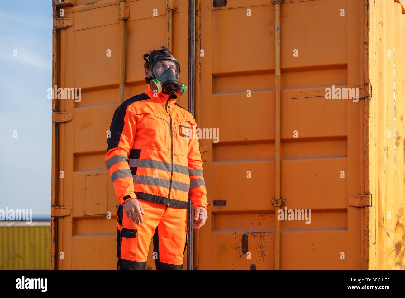 Un travailleur caucasien mi-adulte ajuste un masque respiratoire en expédiant des conteneurs pour la formation à la sécurité des matières dangereuses, la protection industrielle et l'environnement toxique p Banque D'Images