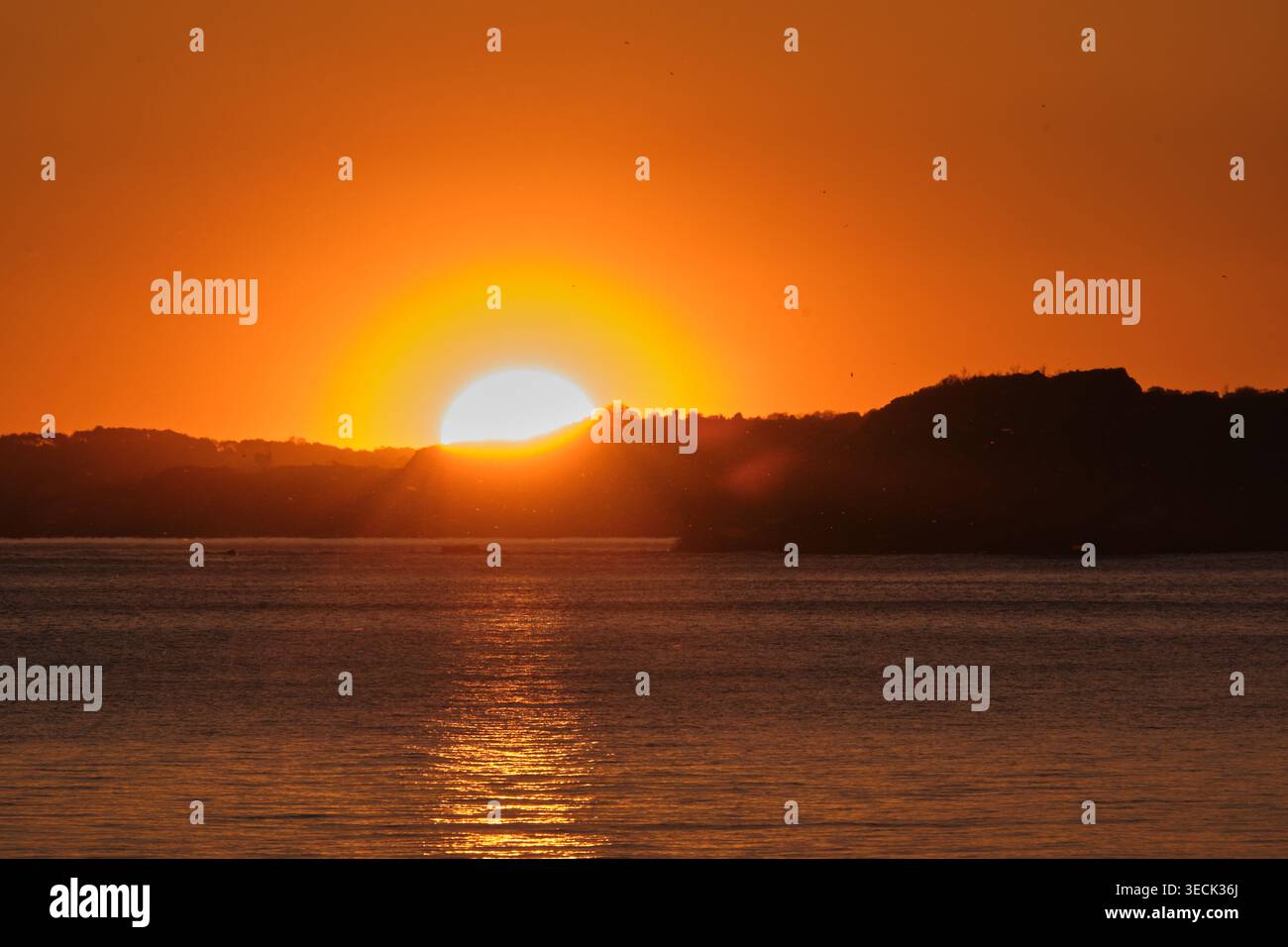paysage où vous pouvez voir un lever de soleil sur la mer, un grand soleil orange se levant des falaises et projetant des rayons vers la mer, une mer calme dans le for Banque D'Images