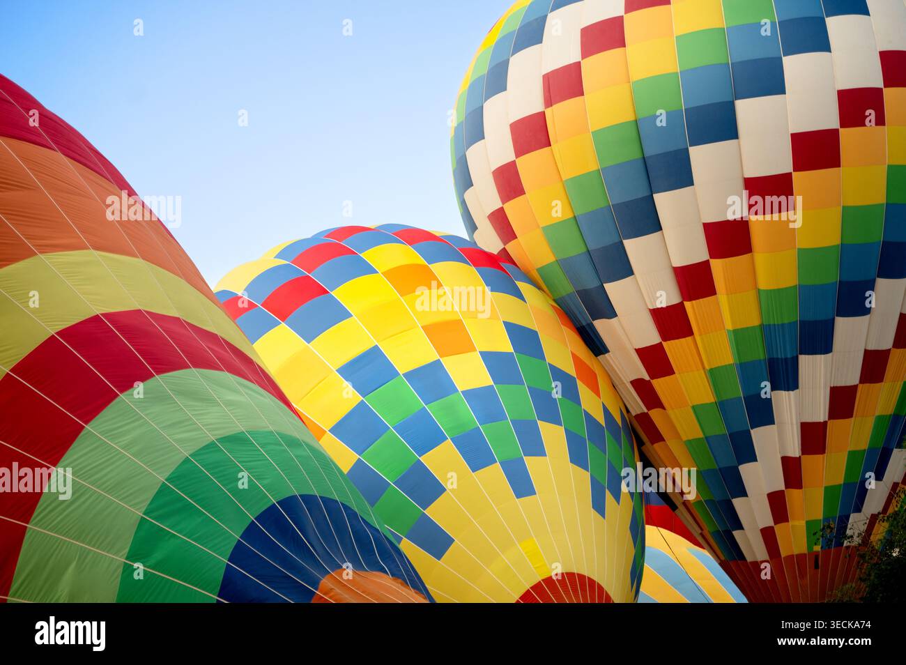 Trois montgolfières colorées s'élèvent ensemble lors d'un vol ensoleillé, montrant des motifs patchwork vifs et des textures de tissu vives sur un bleu clair Banque D'Images