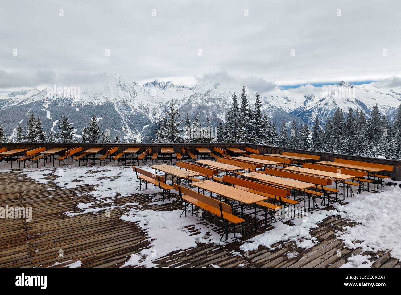 Vue panoramique sur un paysage de montagne enneigé dans les Alpes en mars. Des bancs en bois sur une terrasse donnent sur les sommets majestueux, créant un tranqui Banque D'Images