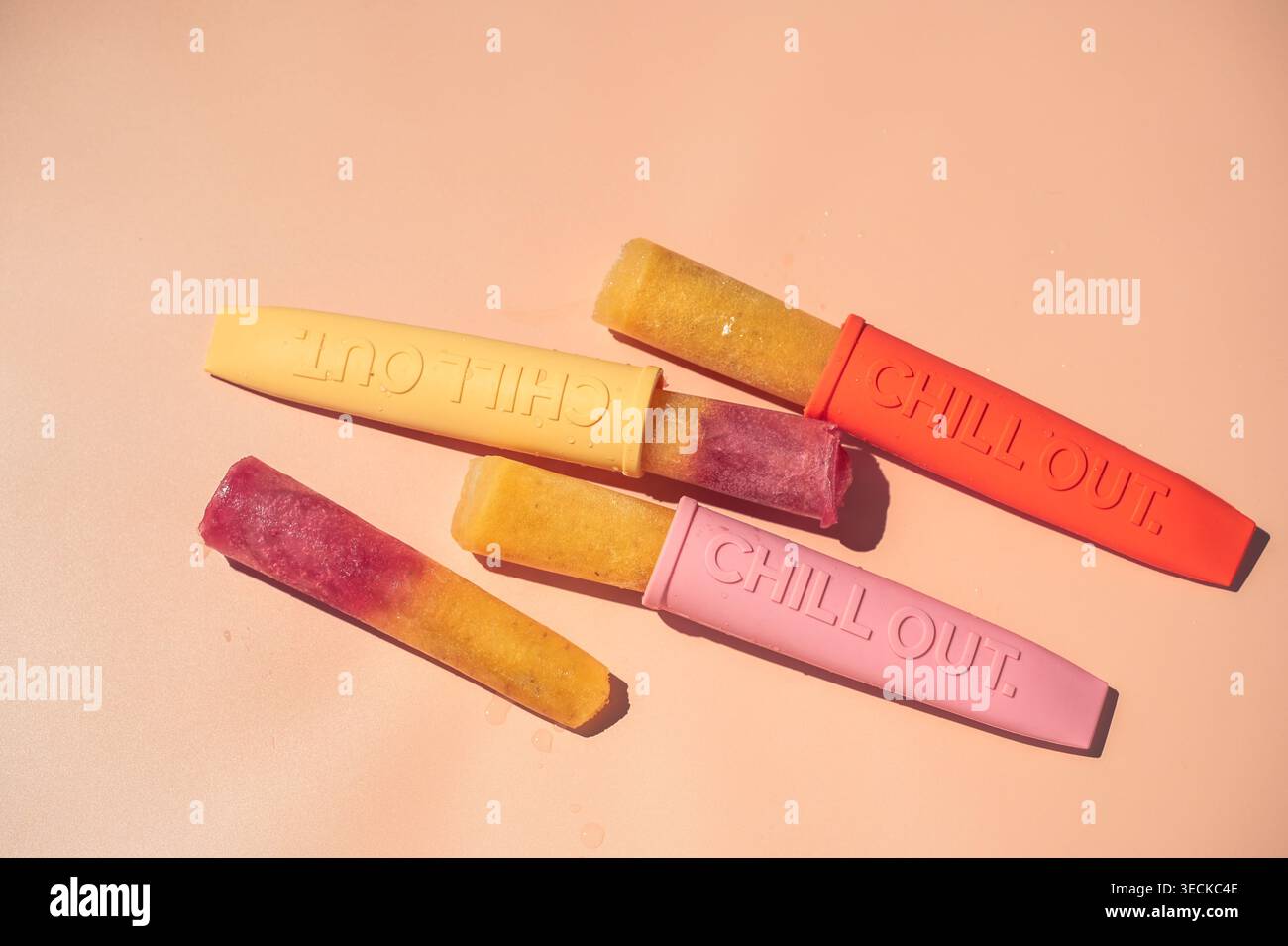 Popsicles de glace aux fruits maison colorées dans des moules en silicone sur un fond pastel, stylisé en pose à plat. Concept de dessert glacé rafraîchissant pour la chaleur estivale Banque D'Images