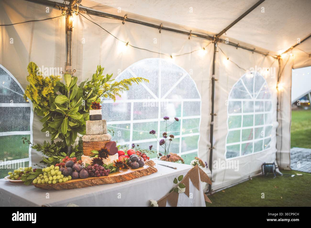 Un beau gâteau à la roue de fromage est exposé avec des fruits frais et des fleurs lors d'une réception de mariage en plein air Banque D'Images