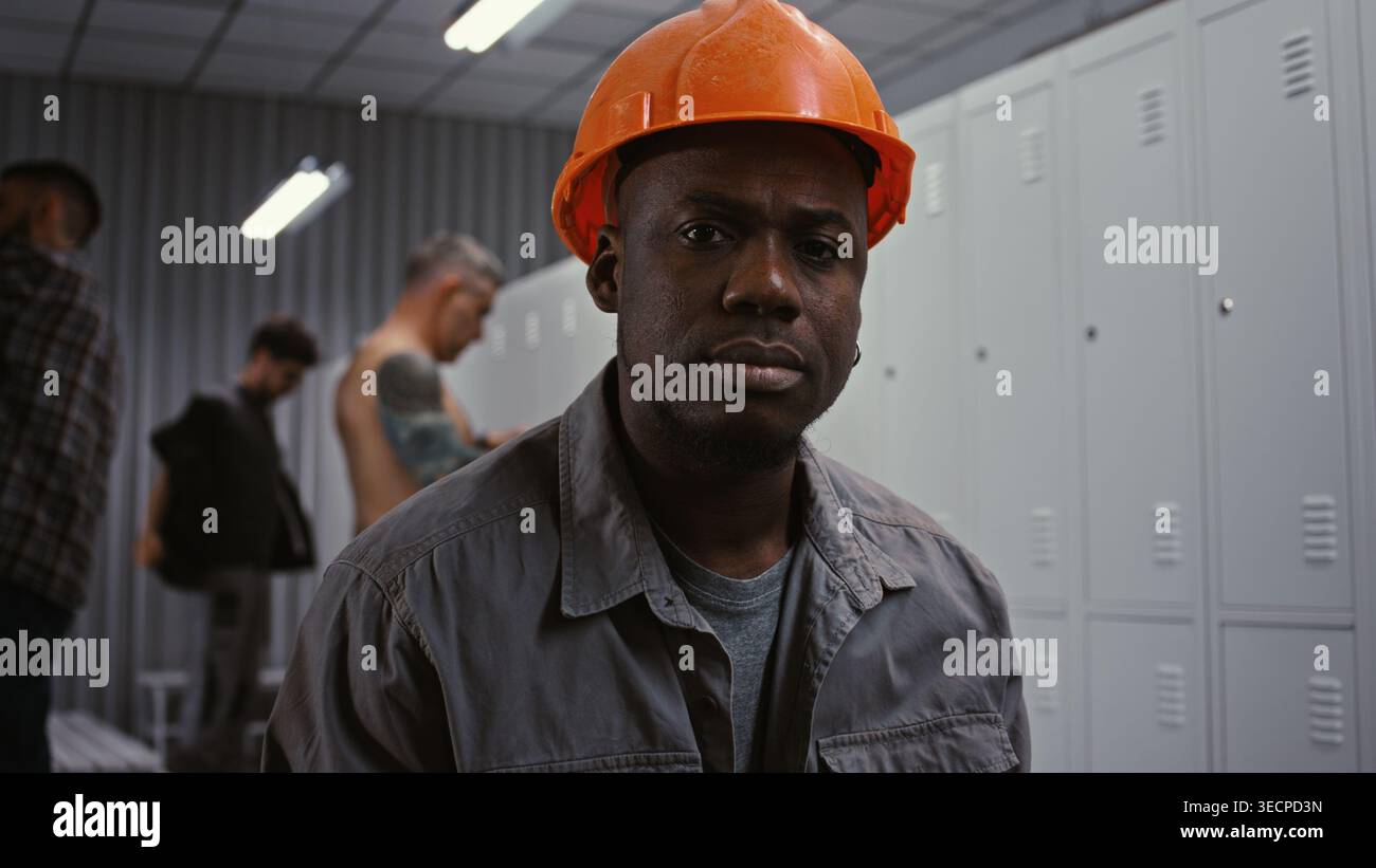 Portrait d'un travailleur afro-américain dévoué dans Orange Hard Hat, regardant en toute confiance dans la caméra avec une expression sérieuse et responsable dans la zone d'habillage. Professionnalisme dans l'industrie lourde. Banque D'Images