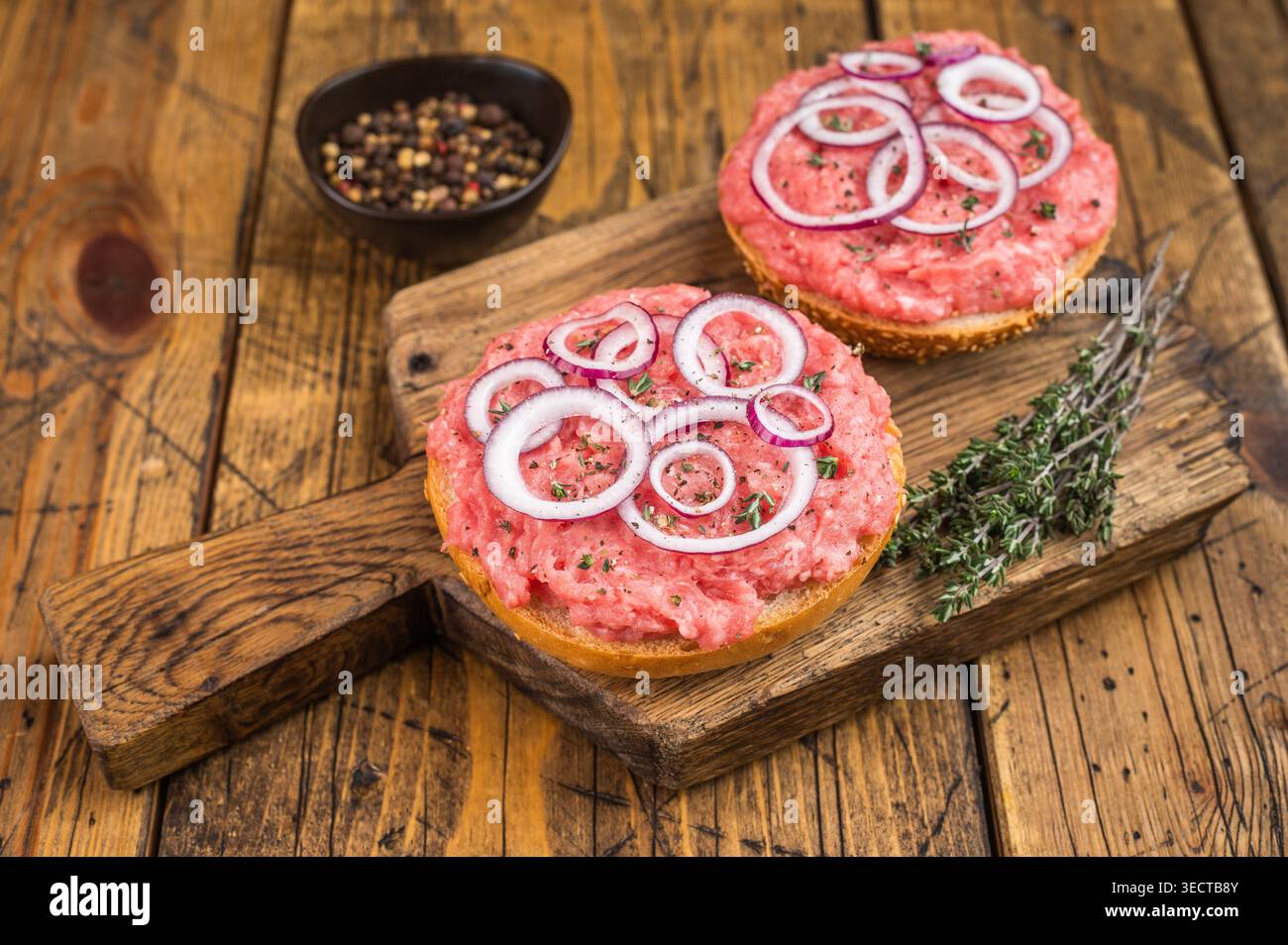Mettbroetchen sandwichs de porc allemand avec porc haché cru étaler des rondelles d'oignon et des herbes sur une planche rustique Banque D'Images
