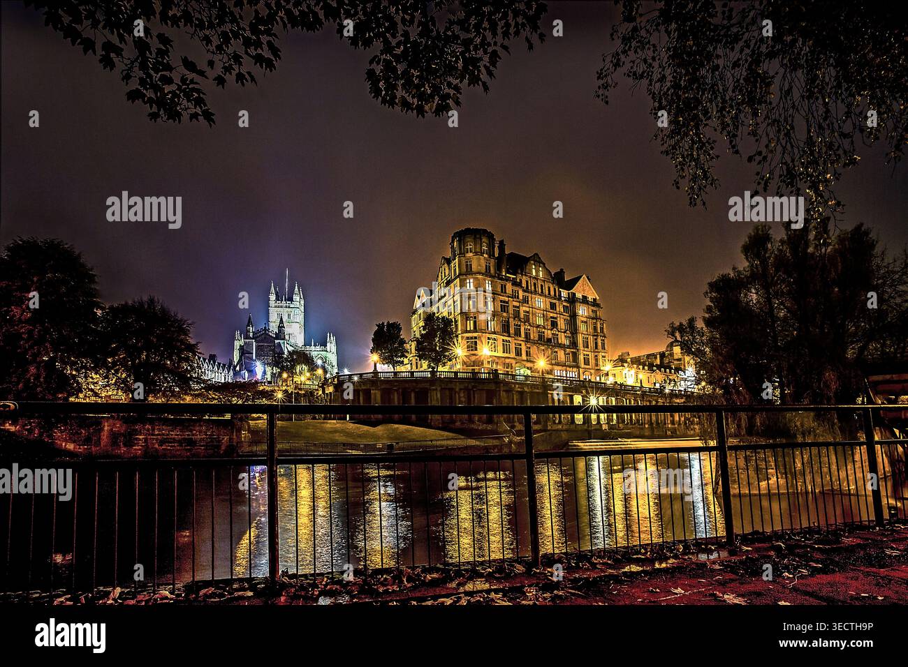 Bain la nuit, avec la cathédrale illuminée et les lumières de la ville projetant des reflets colorés sur la rivière Avon sous les arbres d'automne à une veille tranquille. Banque D'Images