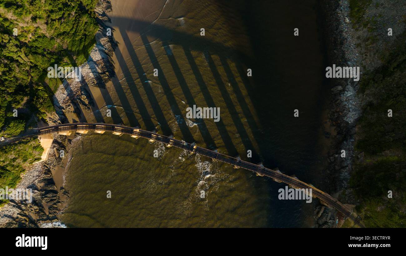Prise de vue par drone aérien d'un pont ferroviaire historique enjambant la gorge de la rivière Kaaimans dans la nature sauvage de Garden route, avec des parois rocheuses couvertes de mousse, flowi Banque D'Images