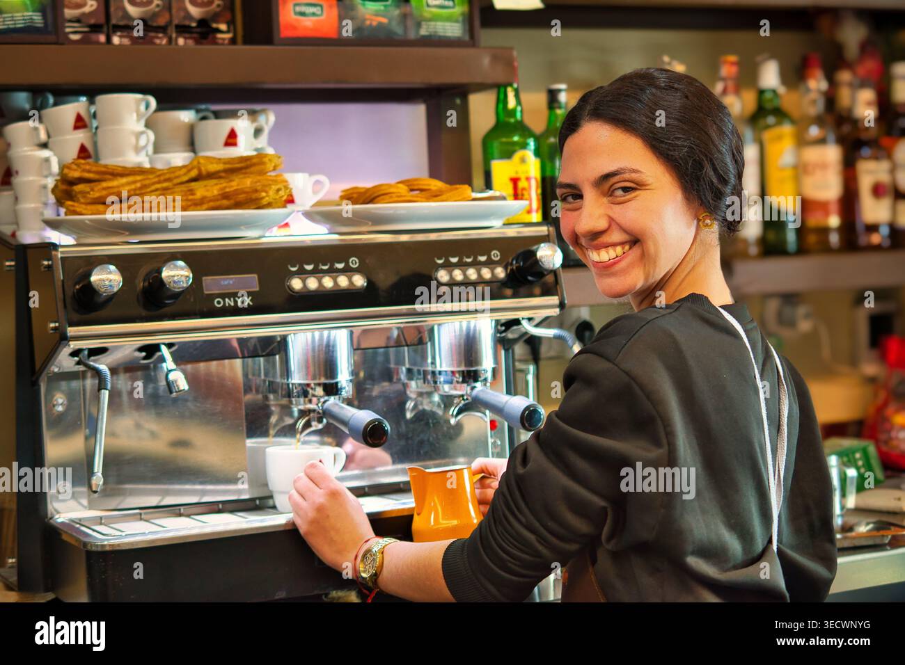 Serveuse versant du lait dans une tasse à café dans un bar espagnol local. Banque D'Images