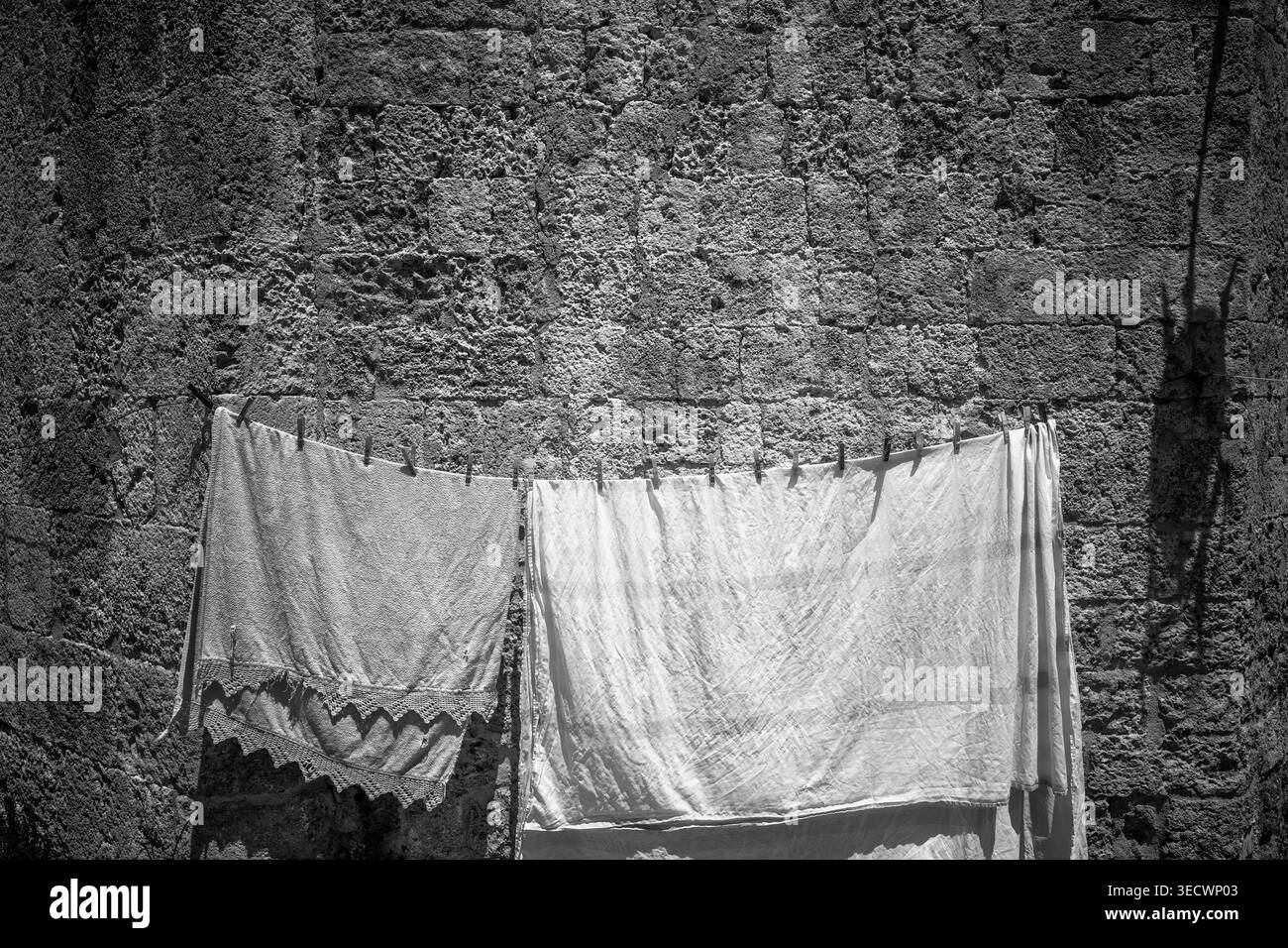 Rhodes, Grèce : deux morceaux de linge textile de couleur claire accrochés à une corde à linge attachée à un mur de maçonnerie en pierre historique texturé, séchant en t Banque D'Images