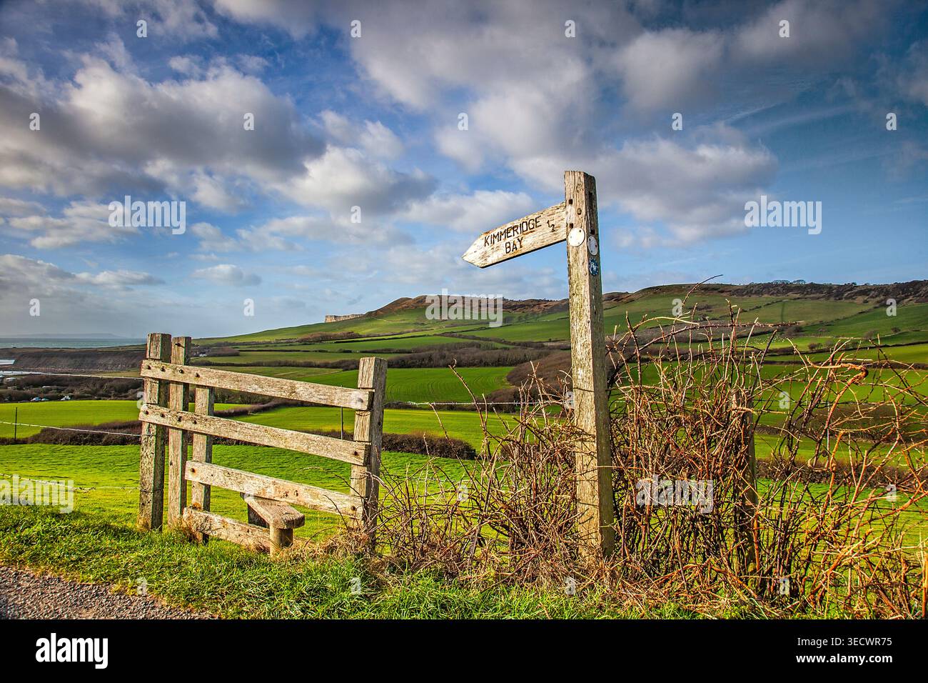 Ancien panneau indiquant Kimmeridge Bay surplombant les collines verdoyantes du Dorset sous un ciel d'été lumineux sur la côte jurassique de l'Angleterre. Banque D'Images