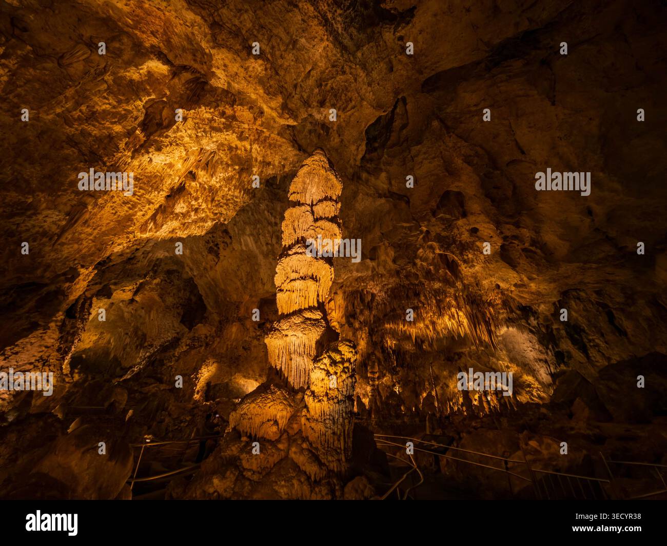 Les stalagmites illuminées et les formations rocheuses coulantes se dressent dans la lueur ambre chaude d'une caverne souterraine. Banque D'Images