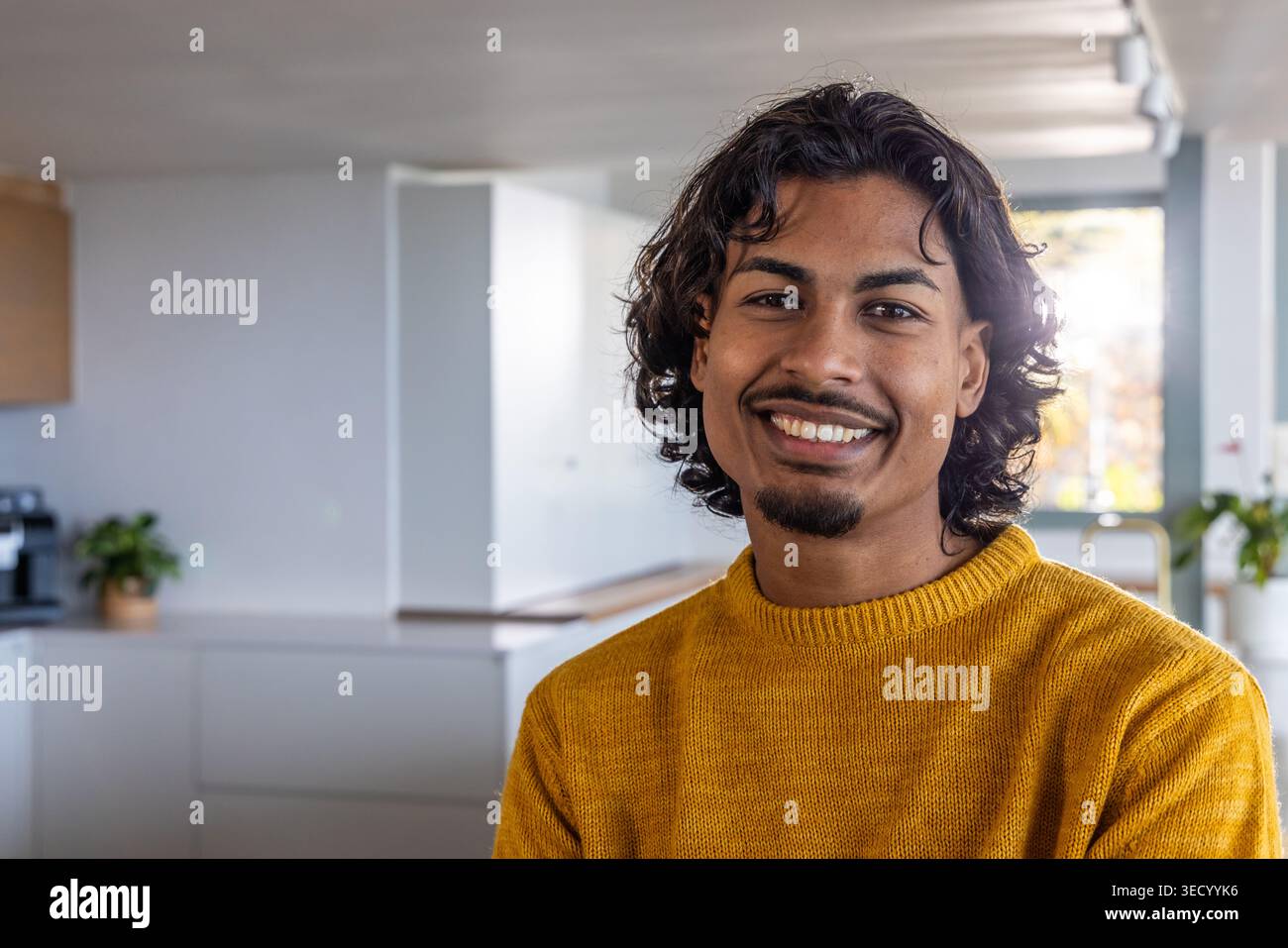 Homme adulte asiatique souriant, debout dans la cuisine moderne portant un pull moutarde près de la machine à café Banque D'Images