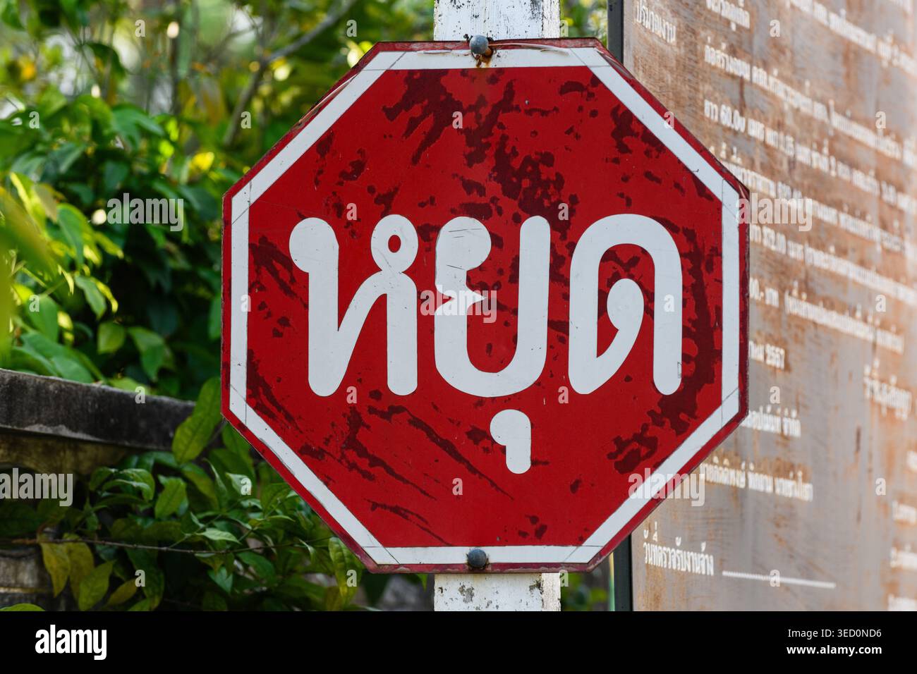 Panneau stop octogonal rouge internationalement reconnu avec le mot « STOP » écrit dans l'alphabet abugida de la langue thaïlandaise. Banque D'Images