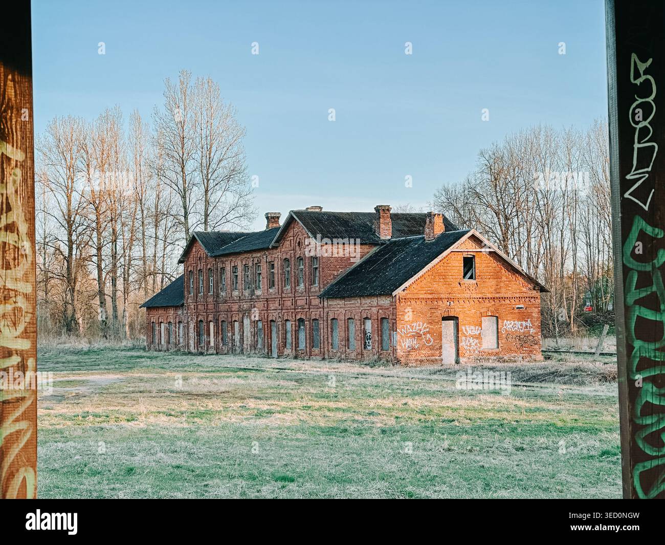 Riga, Lettonie - 30 avril 2026 : ancien bâtiment industriel en briques rouges abandonné dans un champ rural calme, marqué de graffitis et de pourriture. Atmospheri Banque D'Images