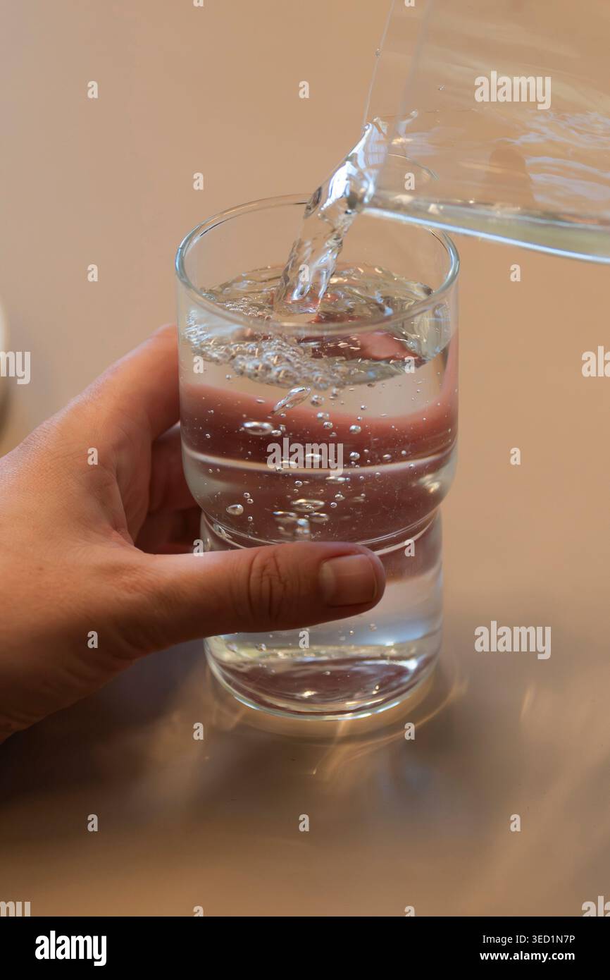 Une main verse de l'eau dans un verre Banque D'Images