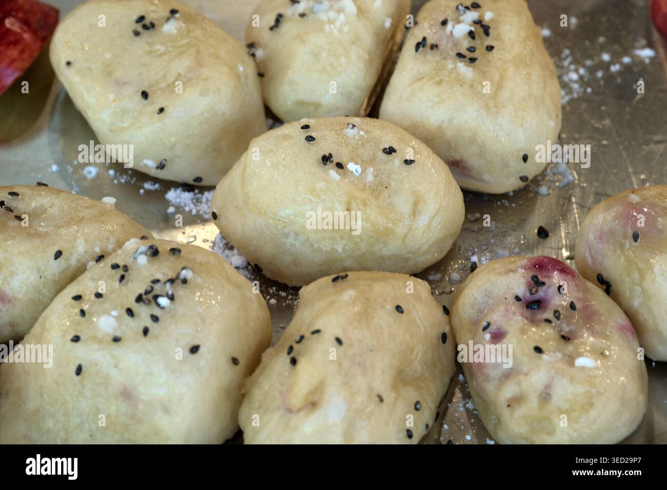 Des boules de pâte molles et rondes reposent sur un plateau, saupoudrées de sésame noir et de sel. Banque D'Images