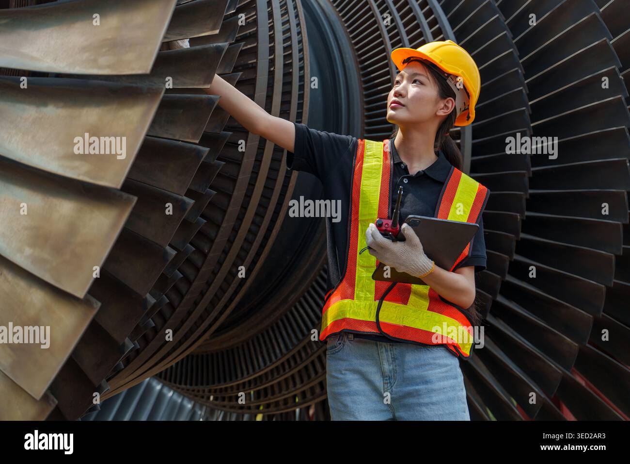La technicienne asiatique d'une vingtaine d'années utilise une tablette numérique pour gérer les dossiers près de grandes aubes de turbine dans une centrale électrique pour la technologie de l'énergie et f Banque D'Images
