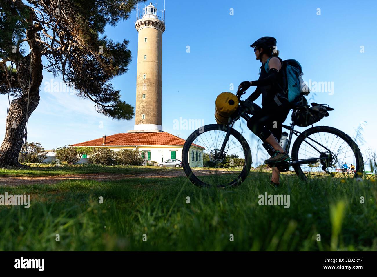 Femme touriste sur un bikepacking, voyage à vélo en Croatie, visite de Dugi otok dans l'archipel de Kornati, aventure à vélo, grand phare à l'arrière Banque D'Images