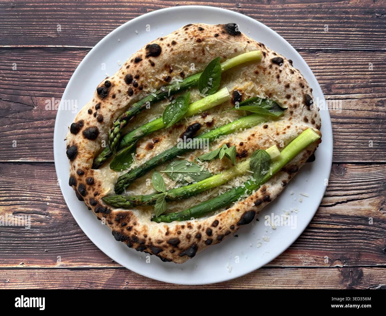 Pizza blanche napolitaine avec asperges, basilic et fromage râpé sur une assiette blanche, vue de dessus sur fond de bois rustique. - Image de stock capturée avec un smartphone