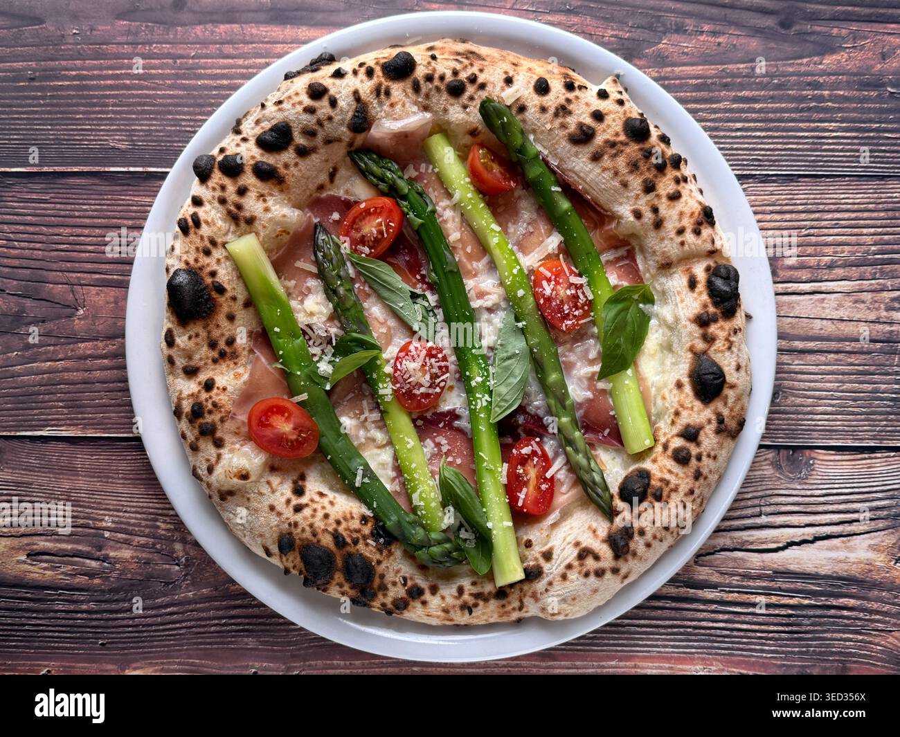 Pizza blanche napolitaine avec asperges, basilic et fromage râpé sur une assiette blanche, vue de dessus sur fond de bois rustique. - Image de stock capturée avec un smartphone