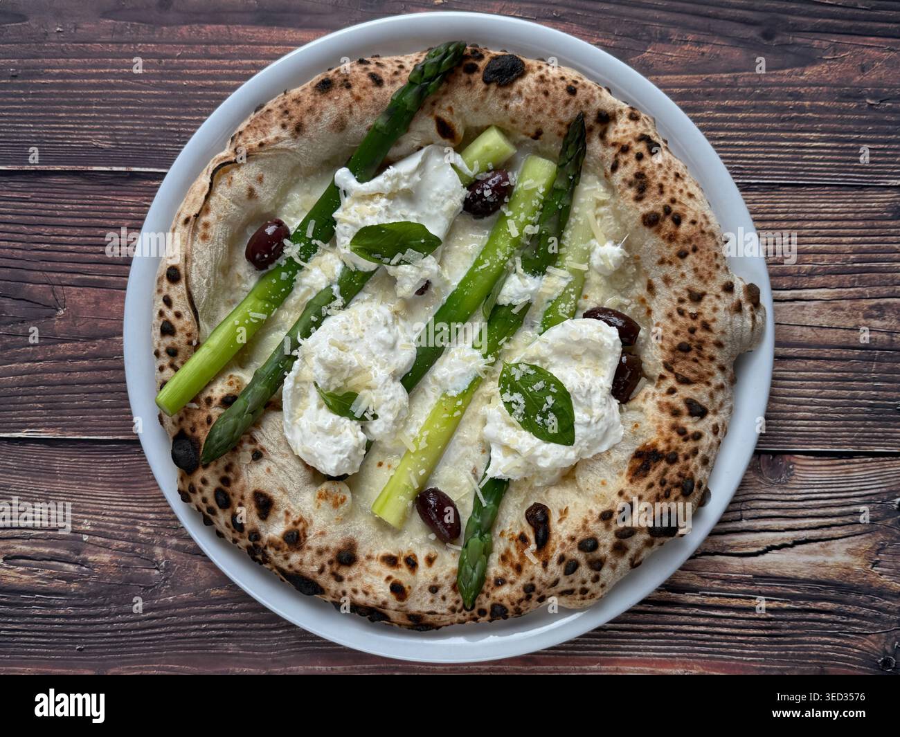 Pizza blanche napolitaine avec asperges, basilic et fromage râpé sur une assiette blanche, vue de dessus sur fond de bois rustique. - Image de stock capturée avec un smartphone