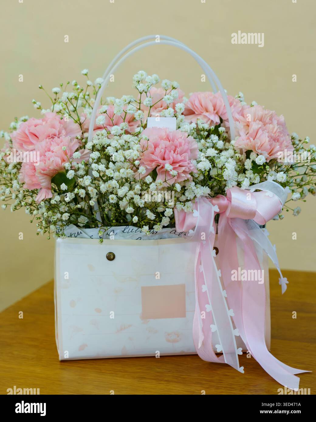Un sac blanc contient des fleurs roses et le souffle de bébé. Il est assis sur une table en bois sur un fond Uni Banque D'Images