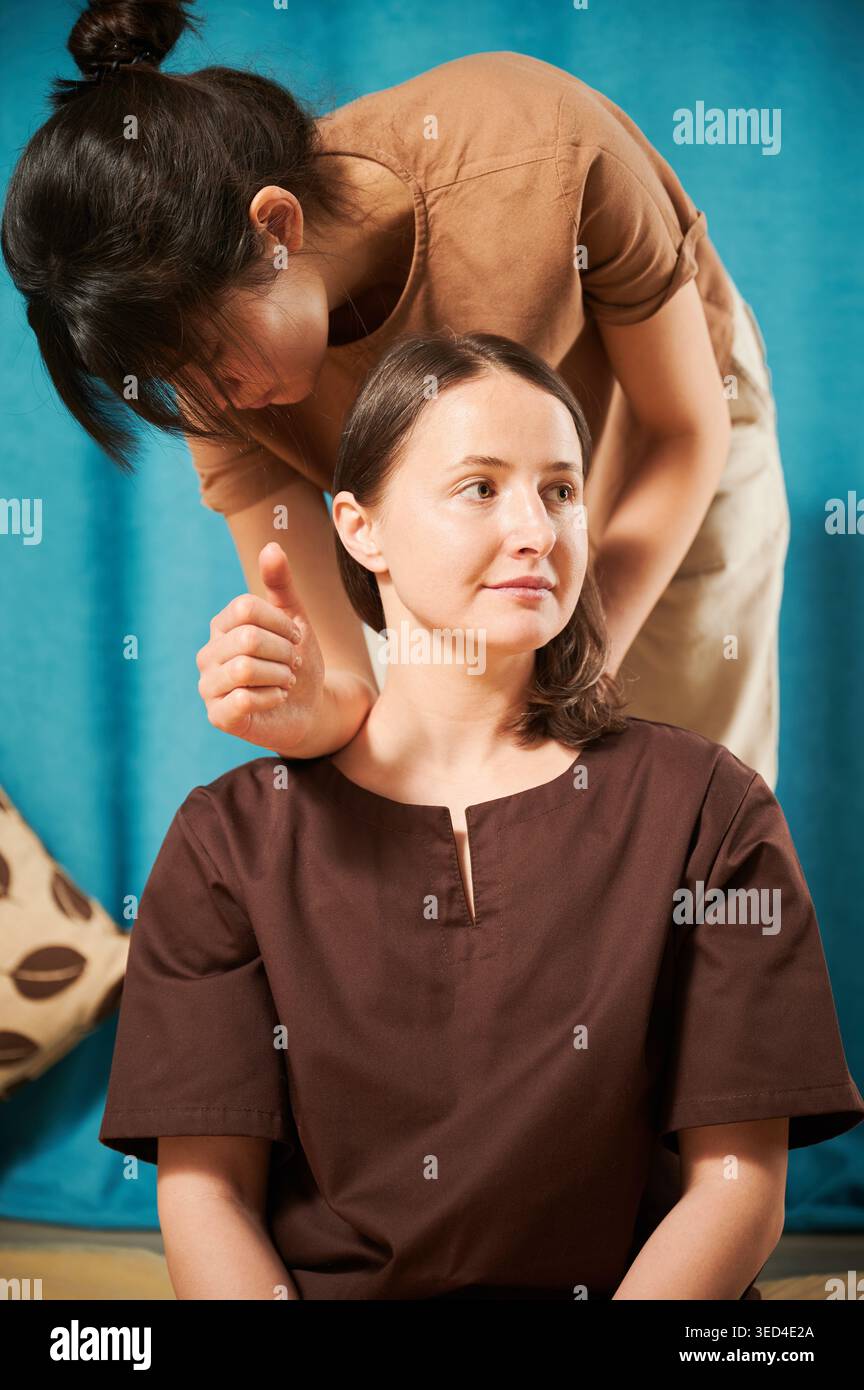 Masseuse faisant massage yoga thaïlandais. Thérapeute de femme faisant le traitement de massage traditionnel pour la patiente féminine à l'intérieur. Client profitant d'un massage des mains dans une atmosphère calme. Banque D'Images