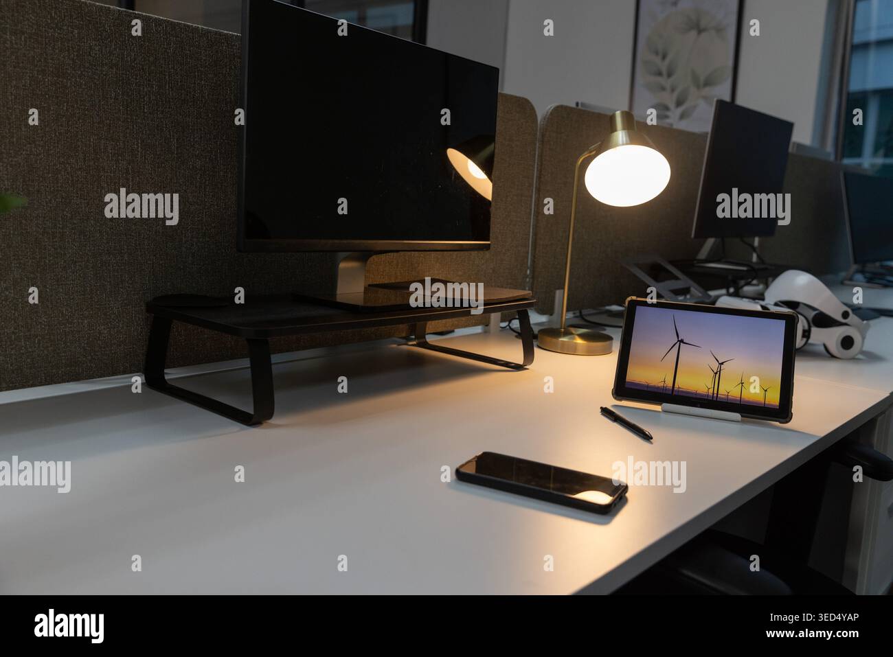 Tablette sur le stand affiche des éoliennes au coucher du soleil sur le bureau blanc, lampe en laiton brillante Banque D'Images