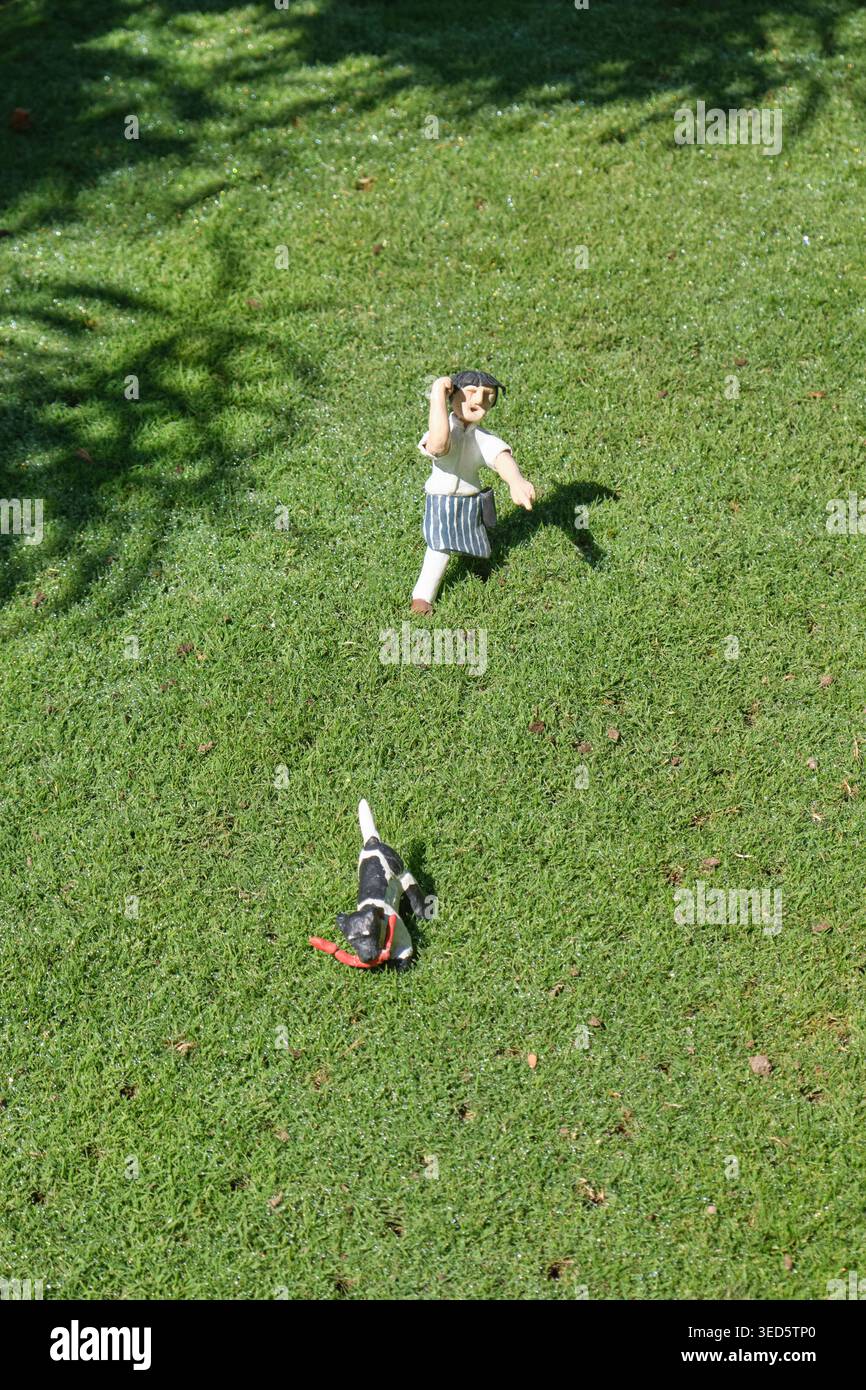 Modèle miniature d'une figure marchant, jouant aller chercher avec leur chien sur une pelouse, l'herbe. Cockington Green Gardens, Canberra, Australie Banque D'Images
