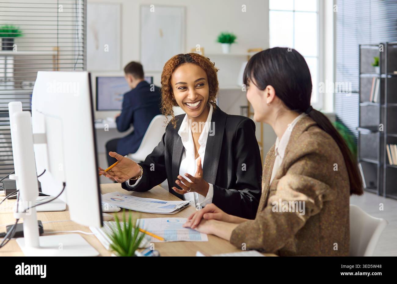 Deux femmes d'affaires collaborant à l'ordinateur pendant la discussion amicale de bureau Banque D'Images